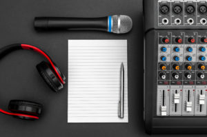 Notepad with audio sound mixer, microphone and headphones on black. Top view.
