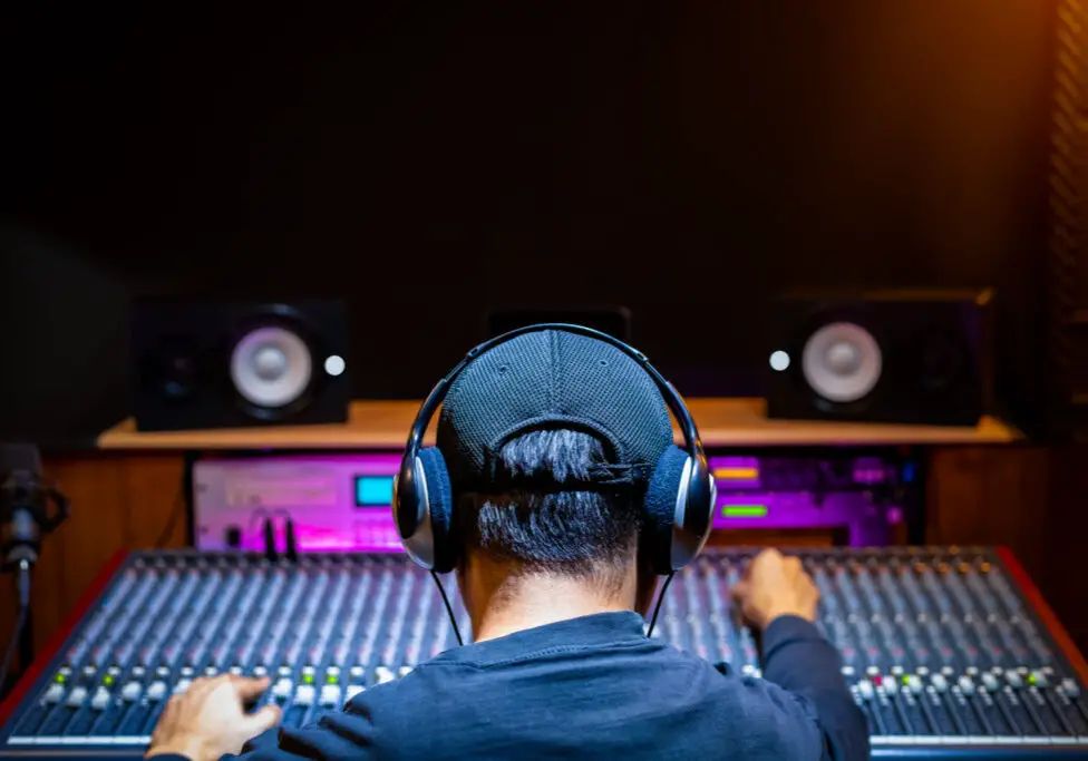 back of asian male professional music producer, sound engineer mixing a song on audio mixing console in recording studio. music production, post production concept